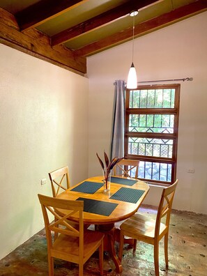 Enjoy meals in this dining area with a table for four, a vase with a plant, and a window offering a view of the surrounding greenery.