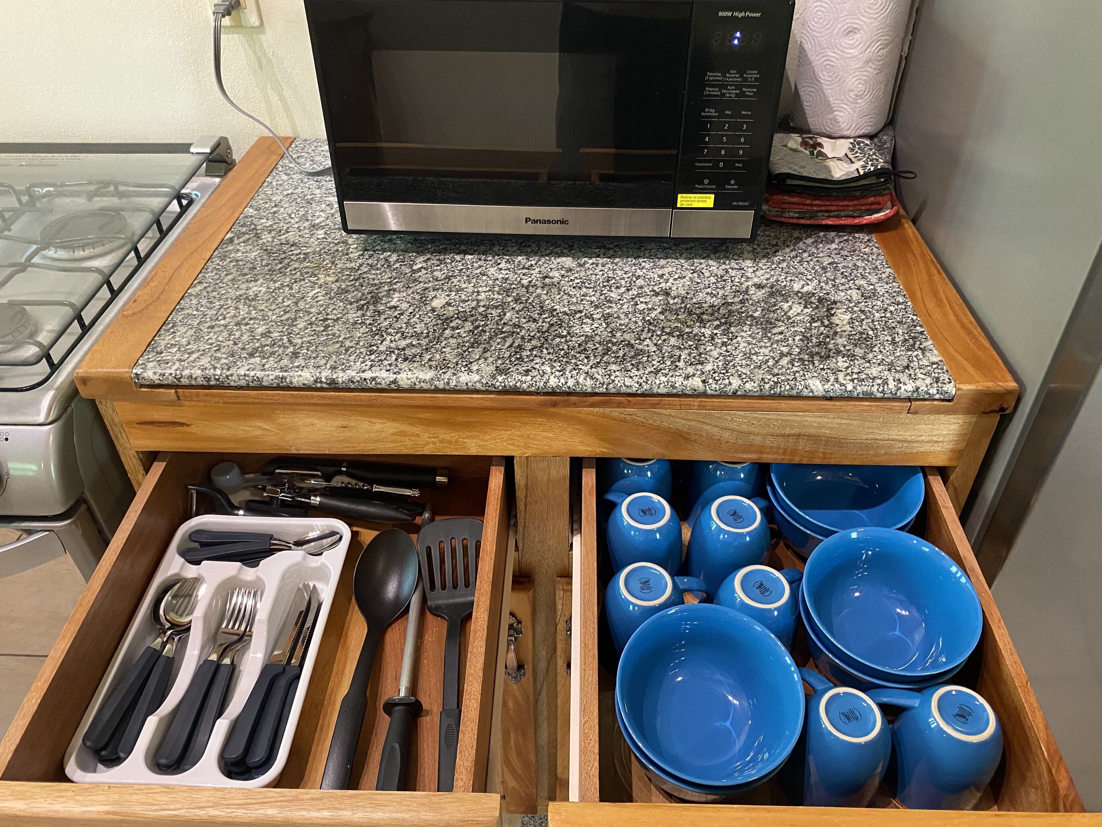 A kitchen with a microwave on a granite countertop, a drawer with utensils, and blue bowls.