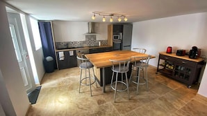 Una cocina moderna con una mesa de madera y taburetes de bar, horno empotrado y microondas.