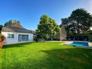 A residential property with a swimming pool, a well-maintained lawn, and a house with a sloped roof.