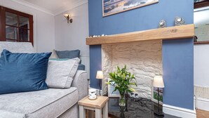 Una sala de estar con un sofá gris, una mesita de madera, un jarrón con flores y una chimenea con pared de piedra.