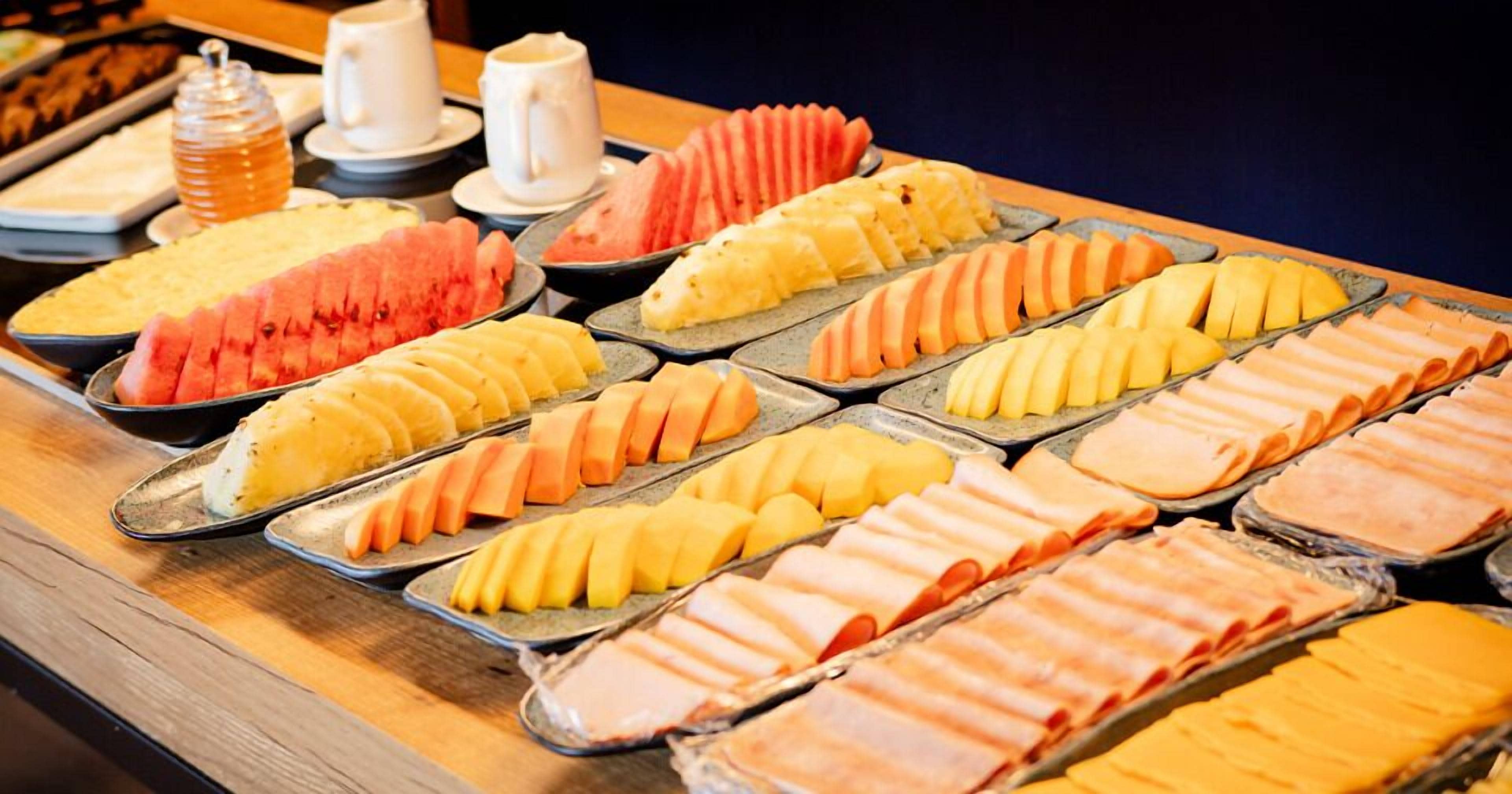 Un bufé con diferentes opciones de comida, incluyendo frutas en rodajas y carnes.