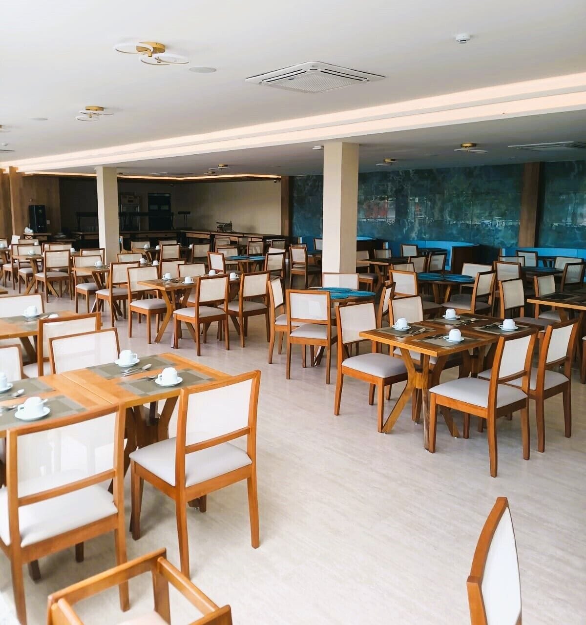 A spacious dining area with multiple tables and chairs, a kitchen in the background, and a large blue mural on the wall.