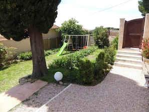 Un jardin avec une balançoire, un arbre et un chemin de gravier menant à une porte.