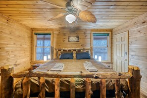 Un dormitorio de cabaña de madera con una cama, un ventilador de techo y una ventana.