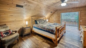 Dormitorio de una cabaña de madera con cama, una silla, una mesita de noche y ventana con vistas al exterior.