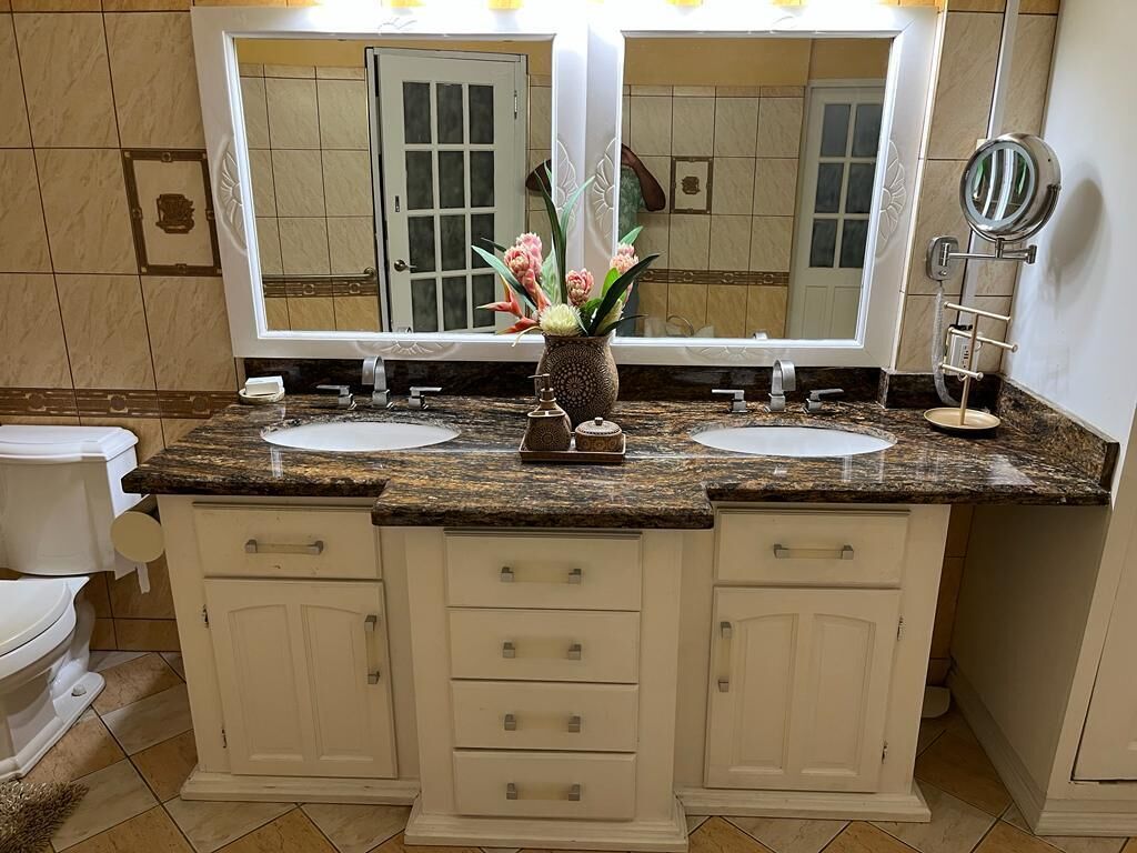 A bathroom with two sinks, a mirror, and a vase with flowers.