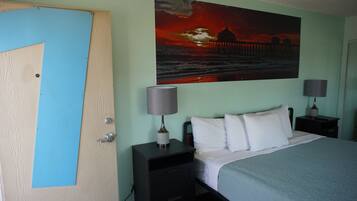 Un dormitorio con una cama, dos mesitas de noche, un cuadro de un atardecer y una puerta.
