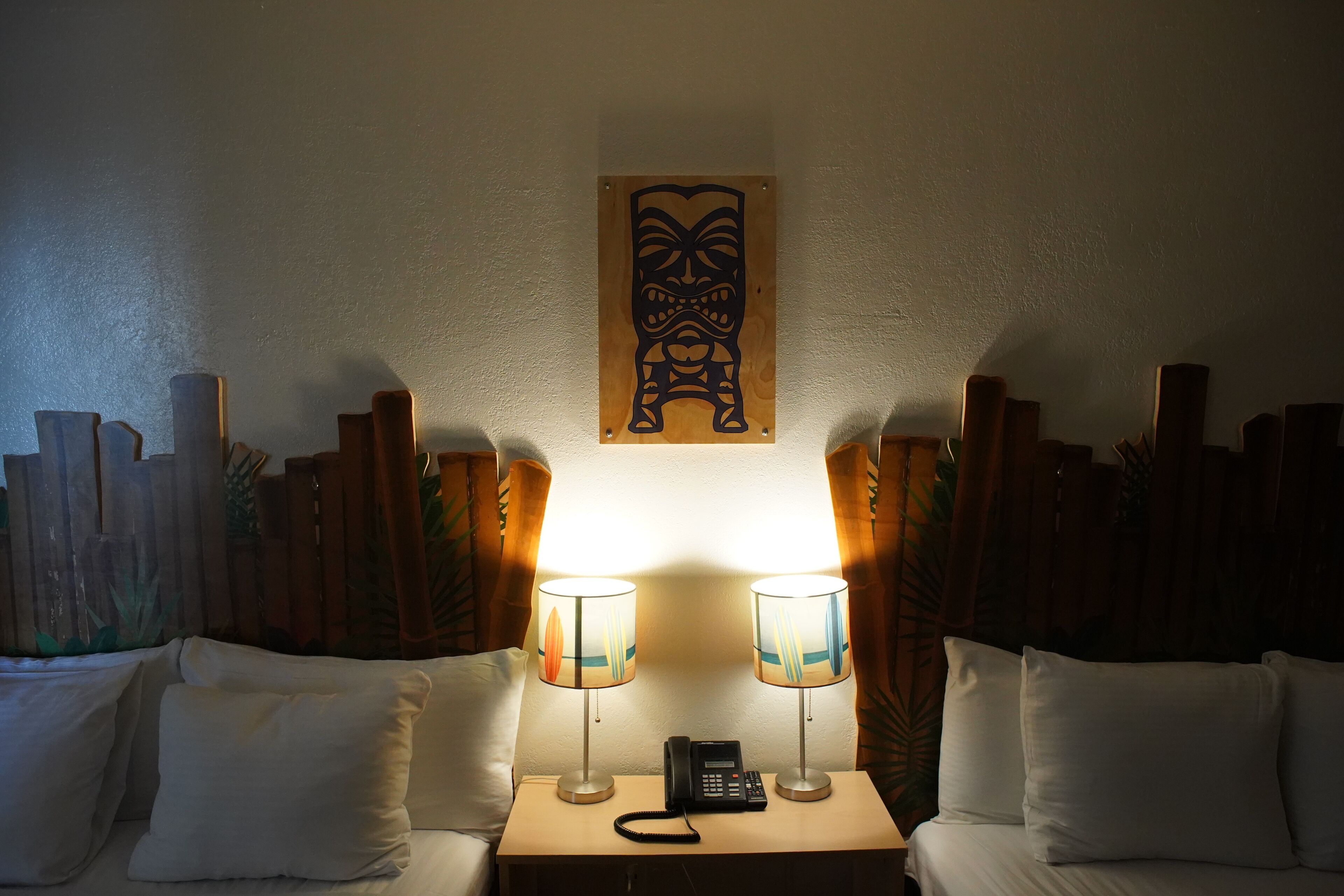 A hotel room with two bedside lamps, a wooden headboard, a wall-mounted artwork, and a telephone on the nightstand.