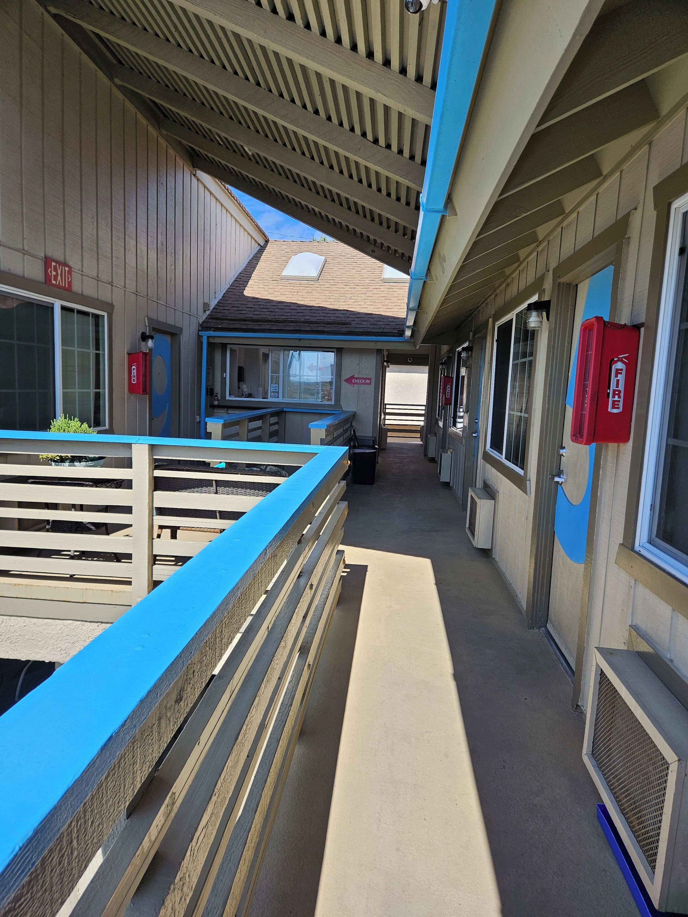 A corridor with a blue railing, a fire extinguisher, and a sign indicating an exit.