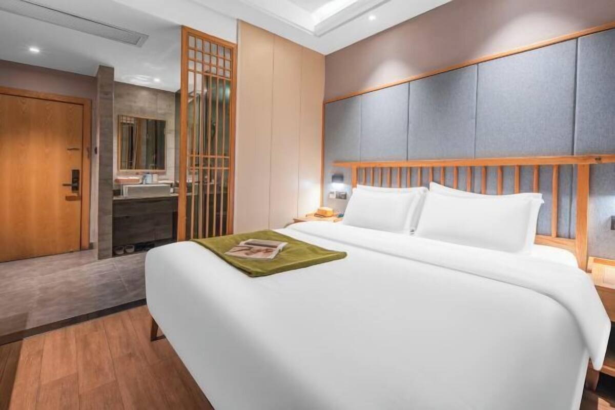 A hotel room with a bed, wooden headboard, a nightstand, a mirror, and a sliding door.