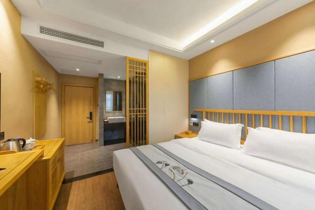 Una camera d'albergo moderna con una scrivania in legno, un letto con biancheria bianca e un'ampia finestra.