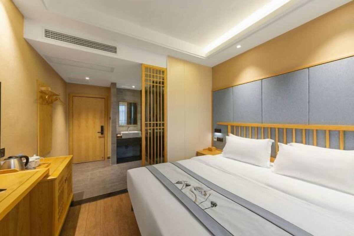 A hotel room with a bed, bedside table, and a wooden dresser.