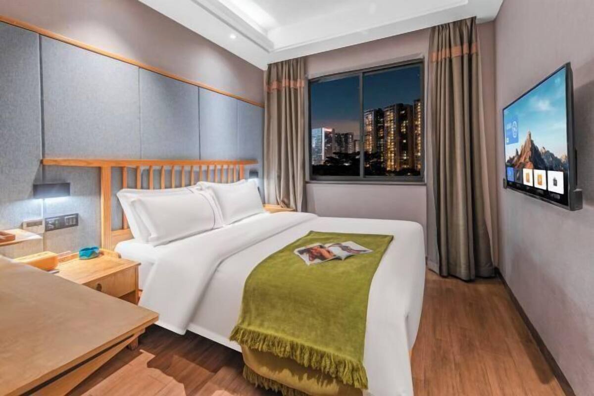 A hotel room with a bed, a desk, a TV, and a window with a city view.
