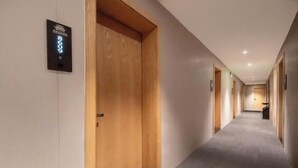 A modern hotel corridor with wooden doors, a digital room number display, and a tiled floor.