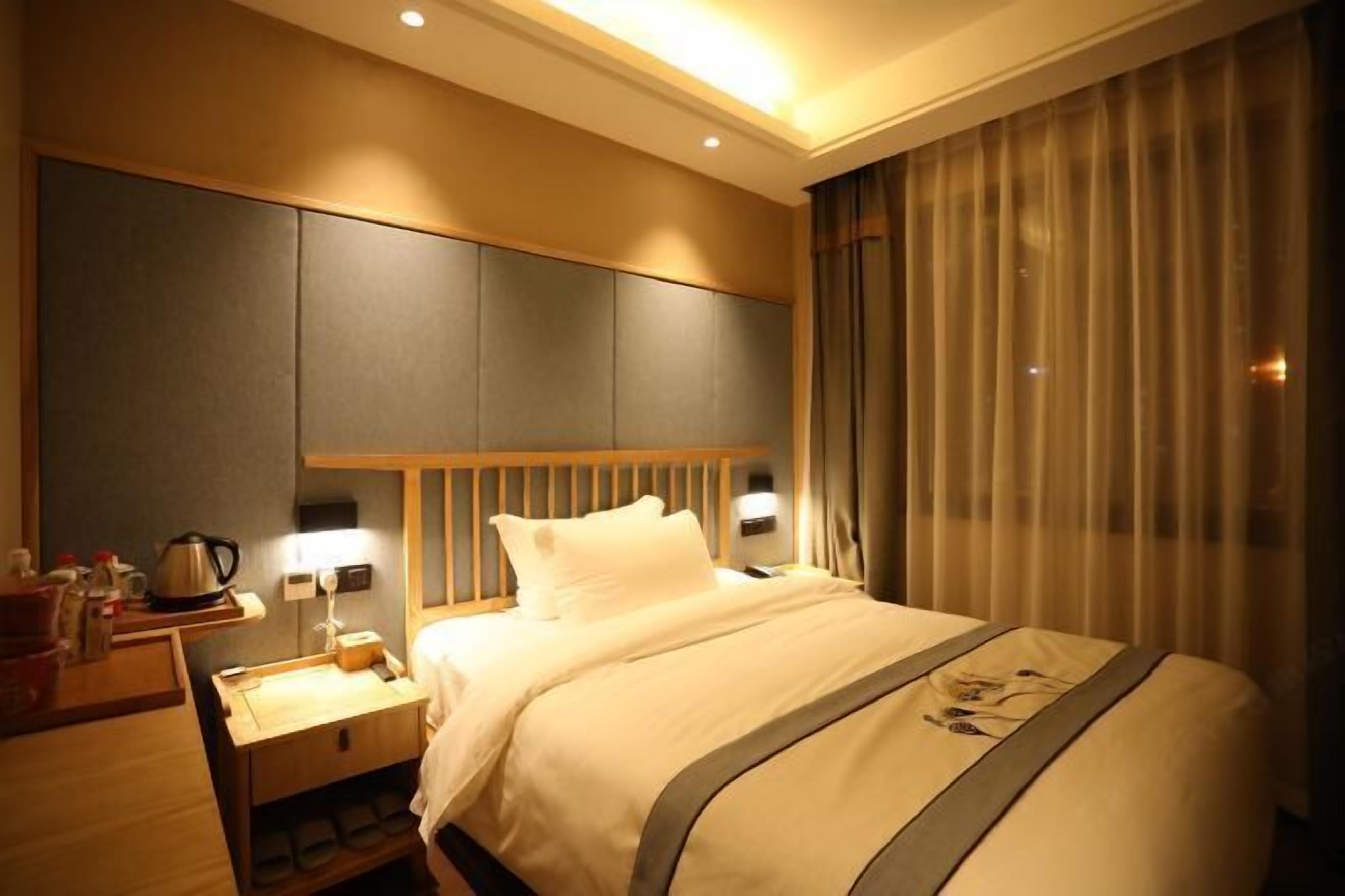 A hotel room with a large bed, a nightstand, a lamp, and a window with curtains.