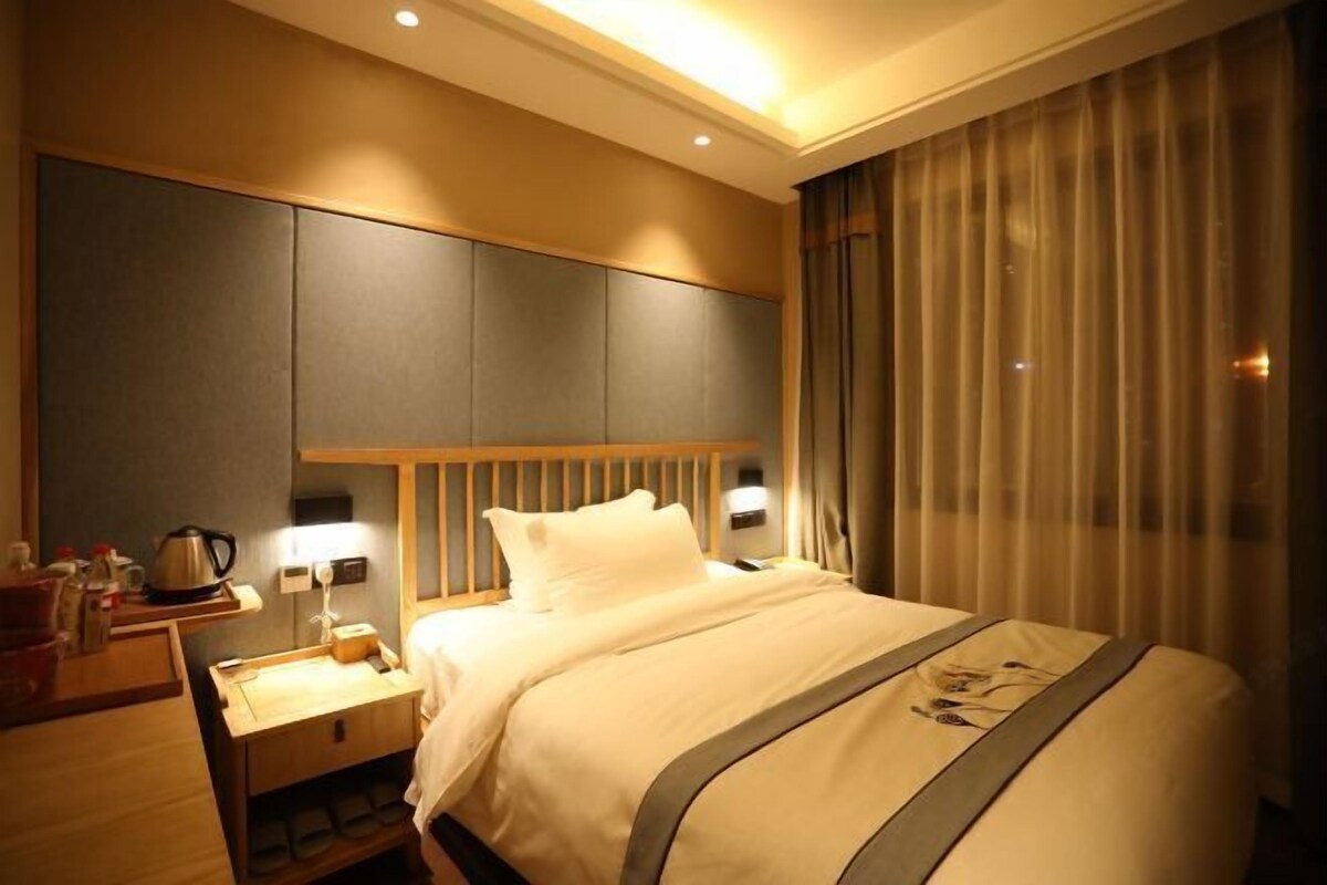 A hotel room with a large bed, a nightstand, a lamp, and a window with curtains.