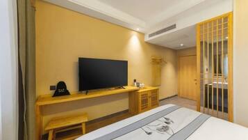 Una habitación de hotel con una cama, un televisor sobre un mueble de madera, un pequeño banco de madera y una puerta corredera con una celosía de madera.