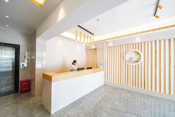 A modern reception area with a receptionist, a reception desk, and a wall with vertical wooden slats. - zhuzijianHotel (Yueyang)