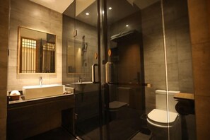 Un baño moderno con ducha envuelta en vidrio, un espejo grande y un lavabo blanco.