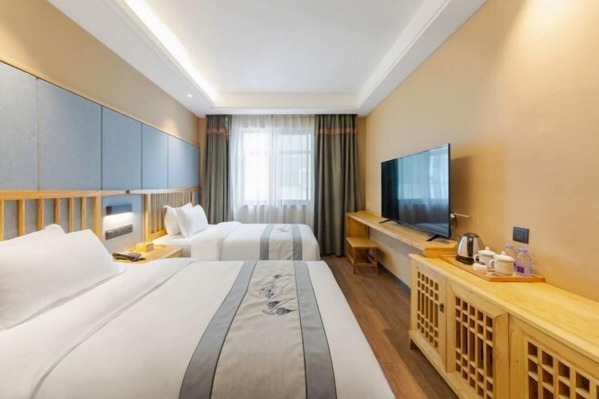 A hotel room with two beds, a TV, a wooden console table, and a large window with curtains.
