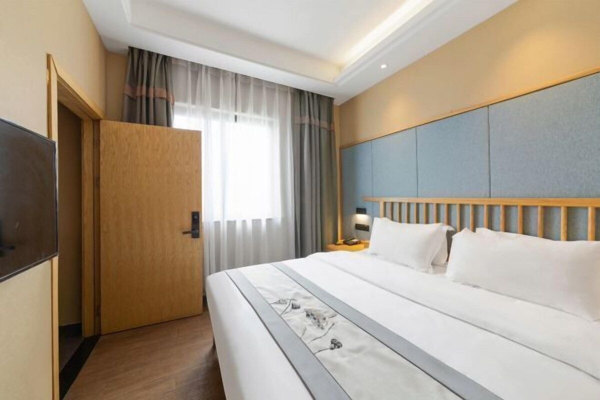 A hotel room with a bed, a TV, a wooden door, and a window with curtains.