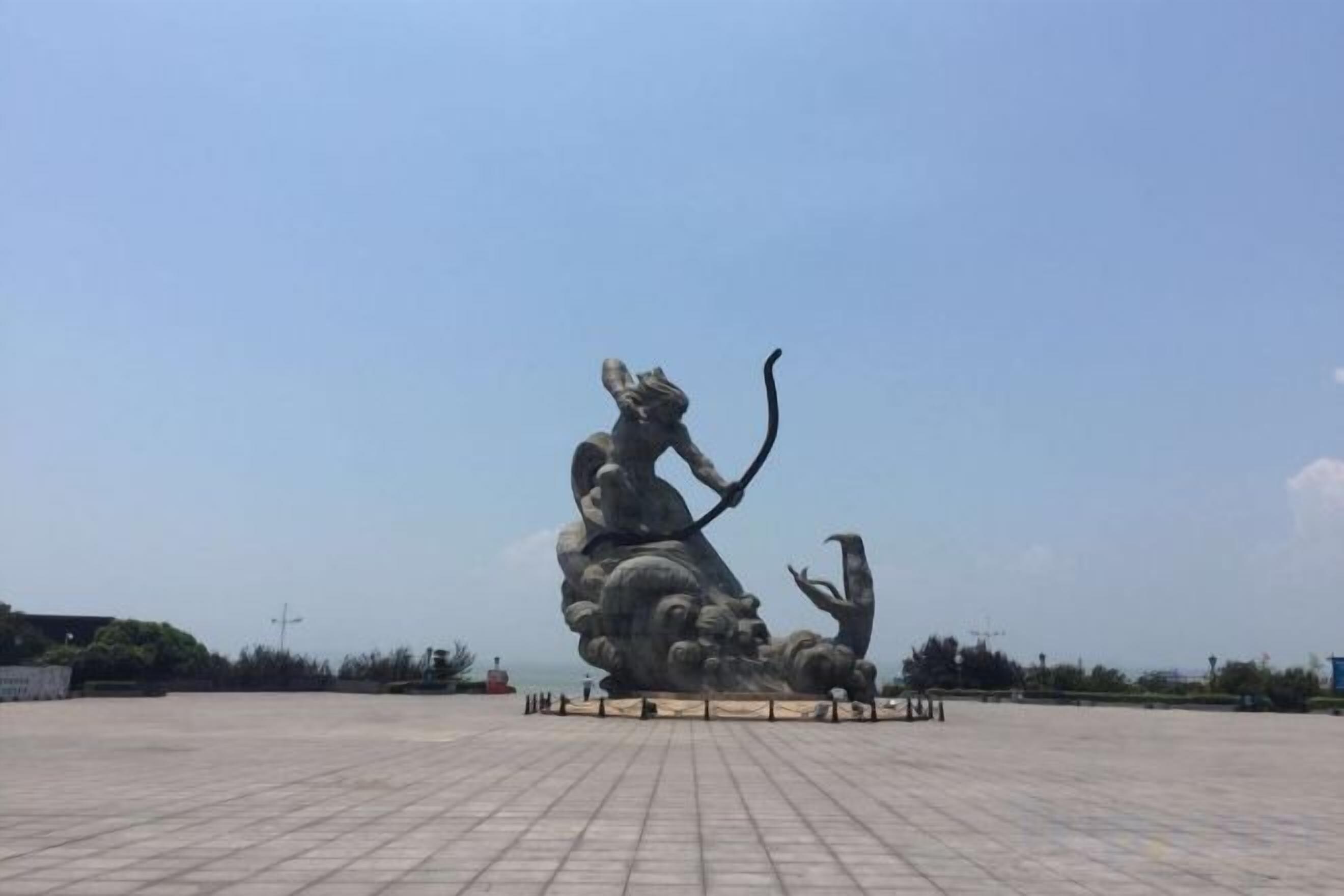 Una gran escultura al aire libre de una figura con arco y flecha, rodeada de una zona pavimentada.