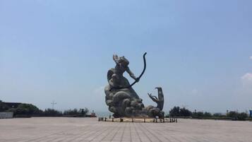 Una gran escultura al aire libre de una figura con arco y flecha, rodeada de una zona pavimentada.