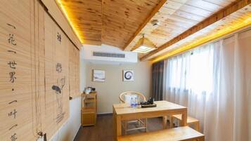 A room with a wooden ceiling, a wooden table with benches, a chair, and a window with curtains.