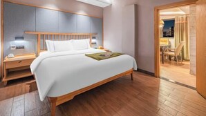 A hotel room with a large bed, wooden headboard, bedside tables, and a view of the city through an open door.