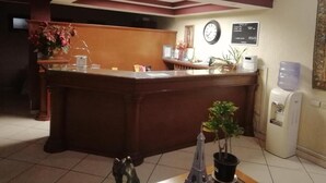 Zona de recepción con mostrador de madera, un reloj, dispensador de agua y una pequeña planta en maceta.