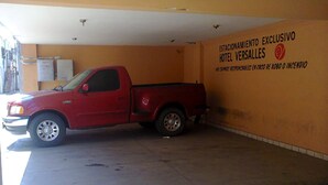 Una camioneta roja estacionada en un garaje con una pared amarilla y un letrero que dice "ESTACIONAMIENTO EXCLUSIVO HOTEL VERSALLES".