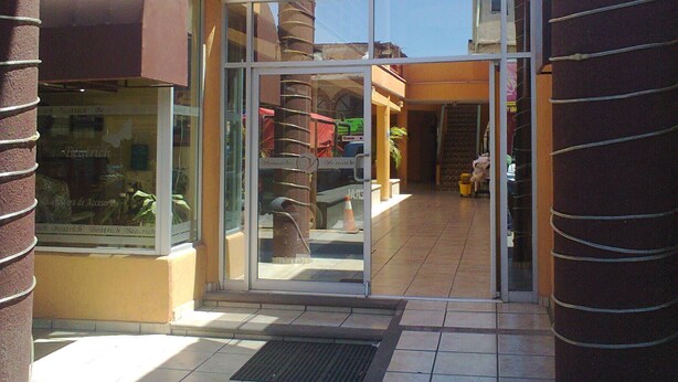 Una entrada de vidrio a un edificio con suelo de baldosas y una escalera central.