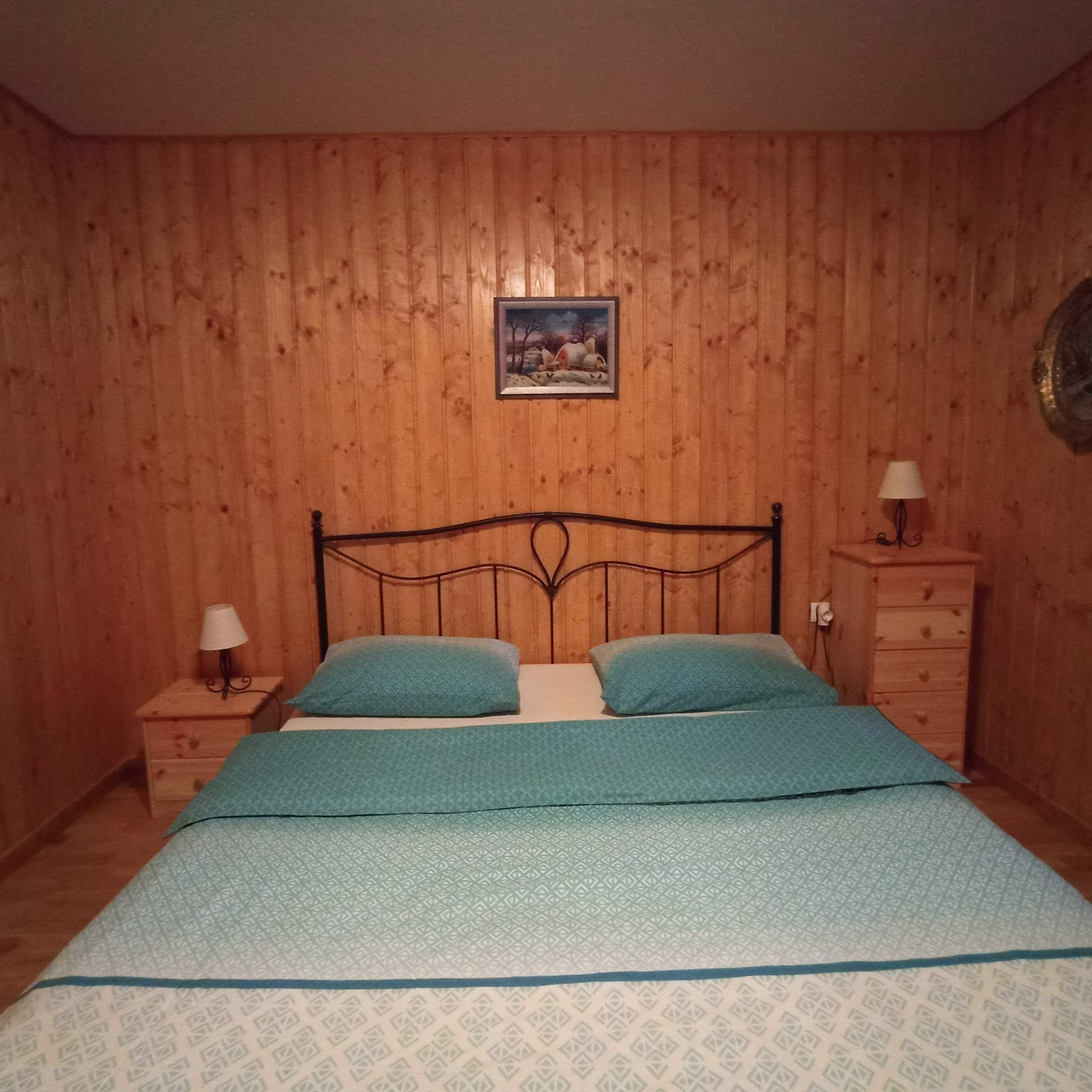 Ein Schlafzimmer mit holzgetäfelter Wand, einem Bett mit zwei Kissen, einem Nachttisch mit Lampe und einer Kommode mit Spiegel.