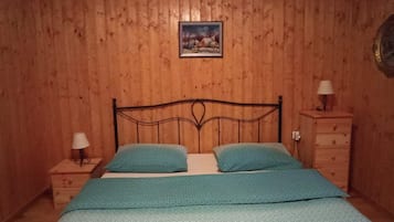 Ein Schlafzimmer mit holzgetäfelter Wand, einem Bett mit zwei Kissen, einem Nachttisch mit Lampe und einer Kommode mit Spiegel.
