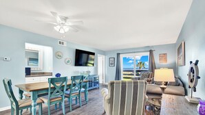 Un salon comprenant un coin repas, un ventilateur de plafond, un téléviseur et une vue sur l’extérieur.