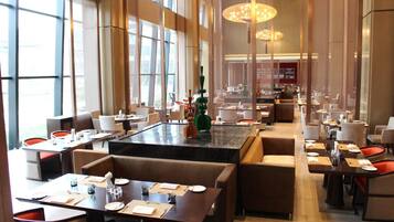 A spacious restaurant with high ceilings and large windows, featuring multiple dining tables and booths.