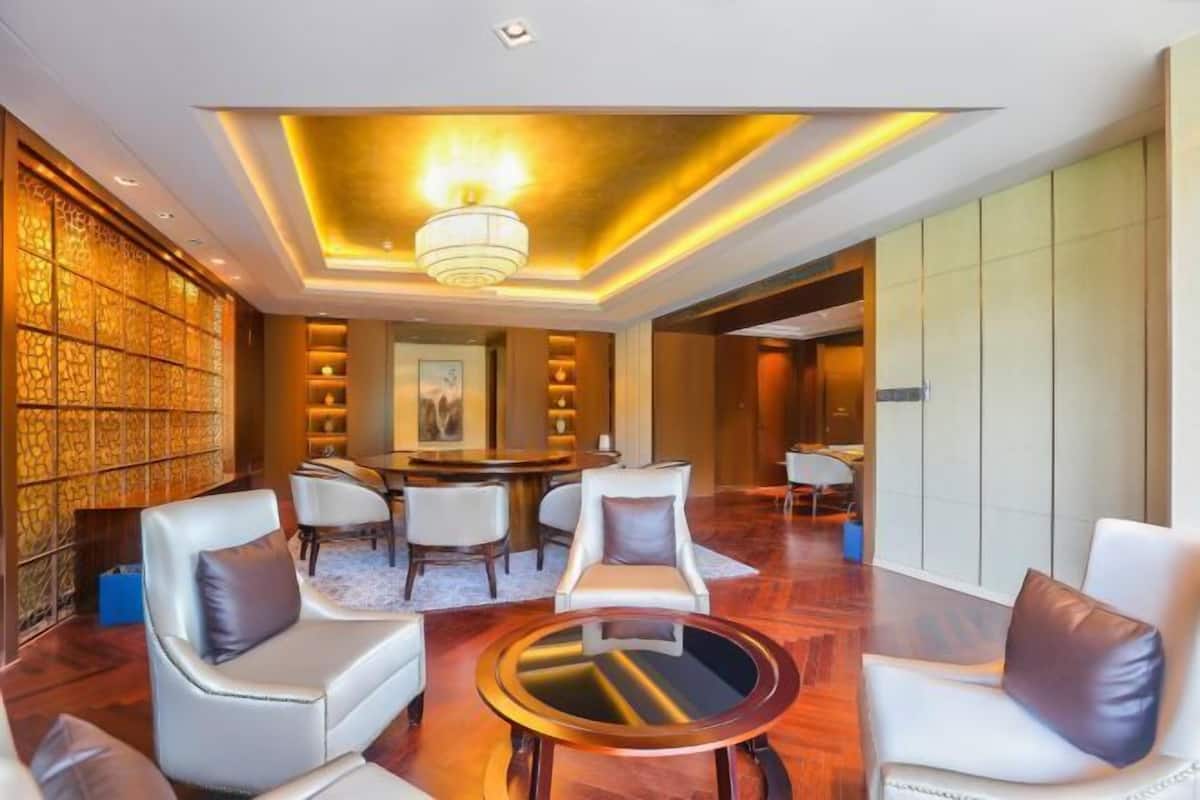 A modern hotel lobby with a round table, white leather sofas, and a decorative wall.