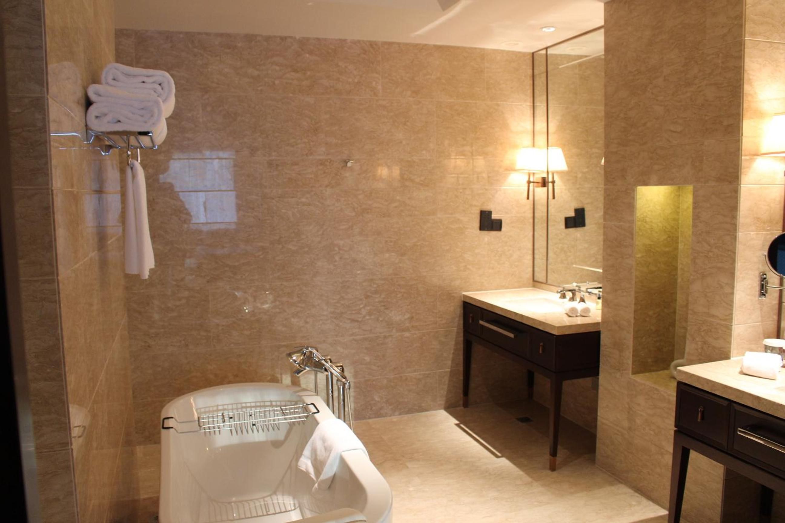 Une salle de bain moderne avec un mur en marbre, un lavabo encastré, un miroir et un porte-serviettes.