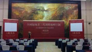 A conference room with a large screen displaying a presentation, rows of tables with chairs, and water bottles on each table.