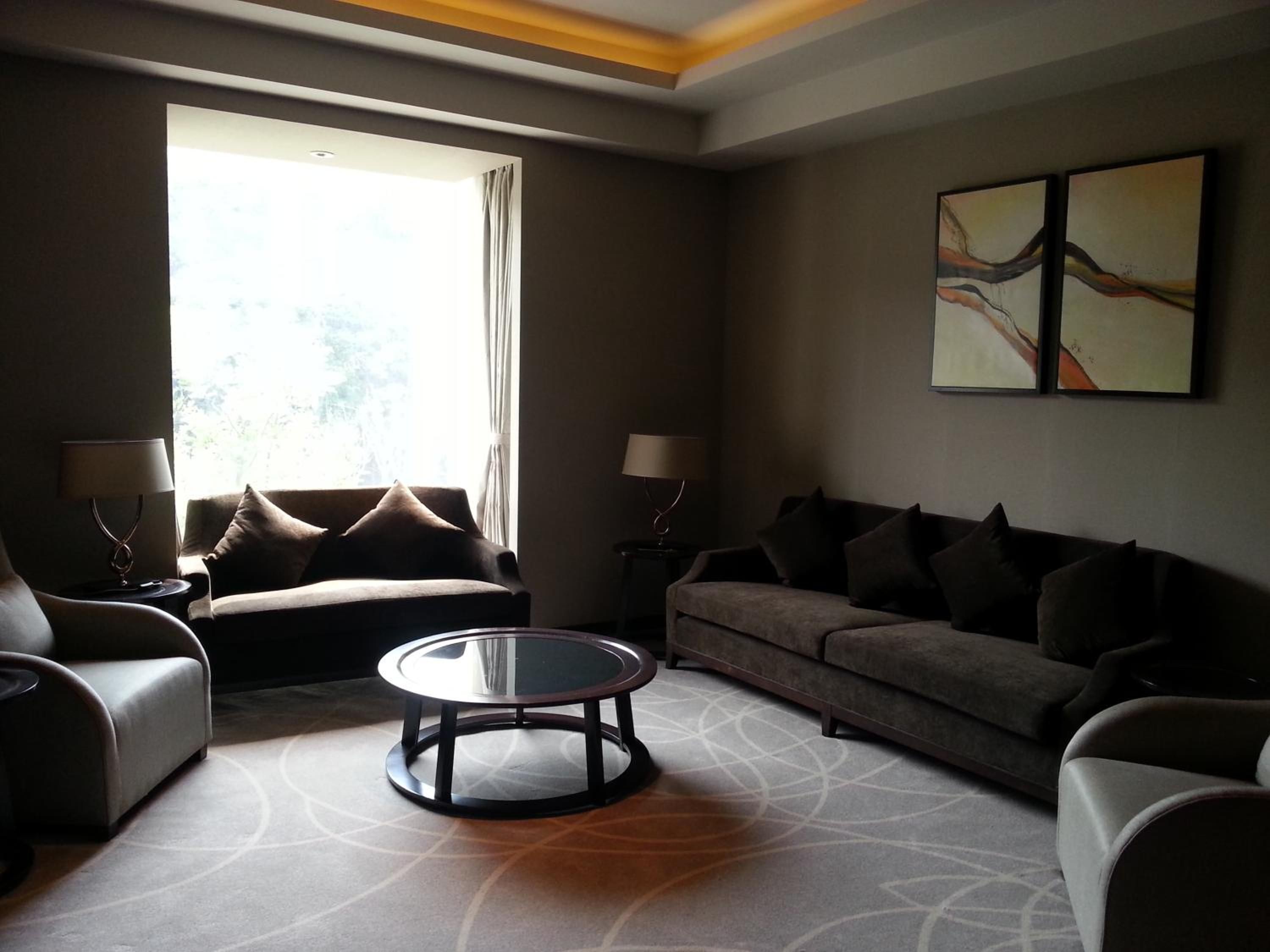A modern living room with a sofa, armchairs, a coffee table, and a large window providing natural light.