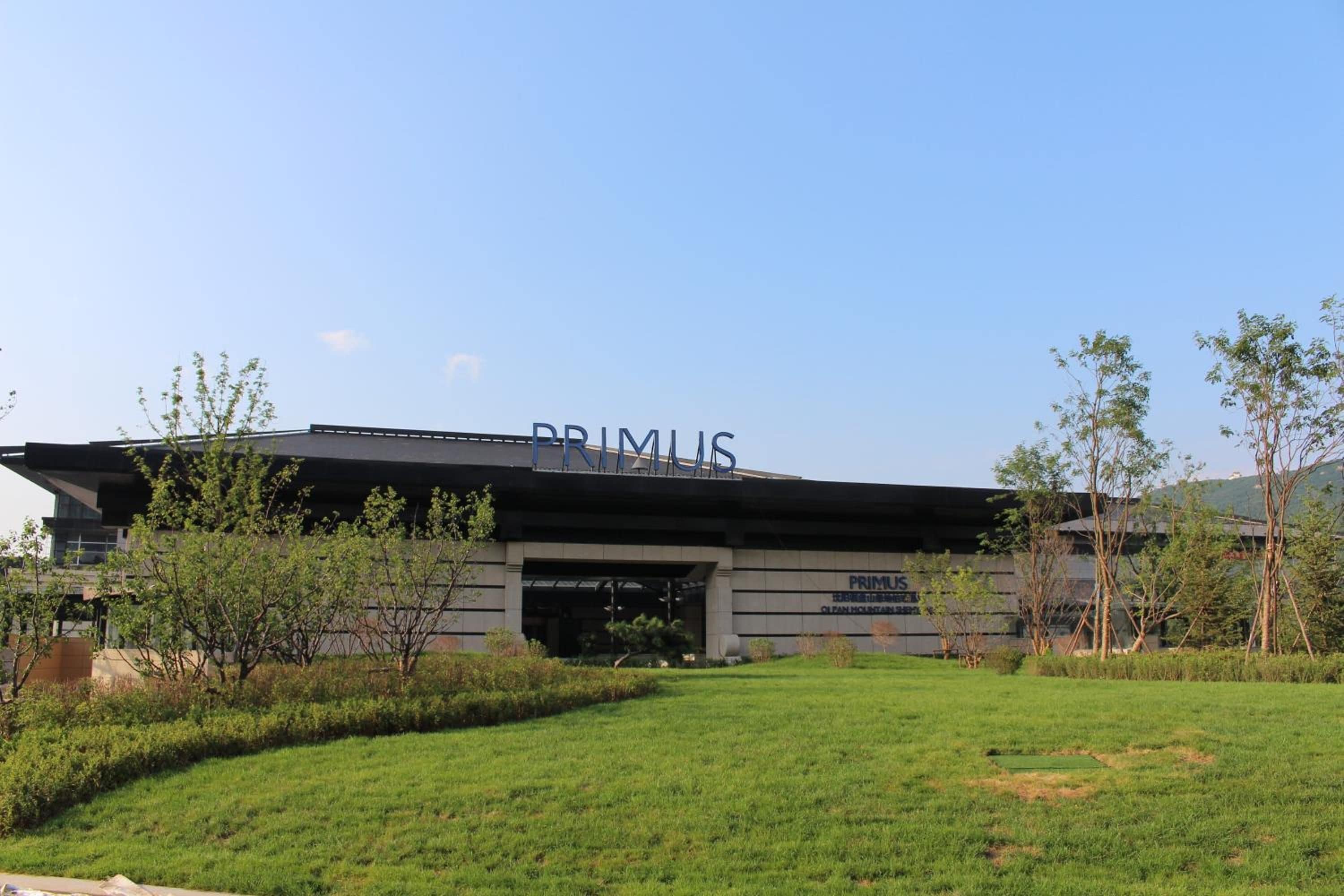 A modern building with the name 'PRIMUS' on the facade, surrounded by a well-maintained grassy area and young trees.