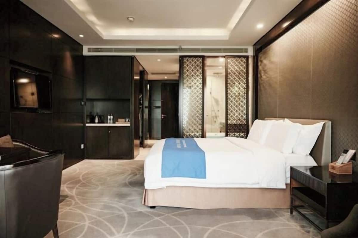 A modern hotel room with a large bed, a desk, a chair, and a TV.