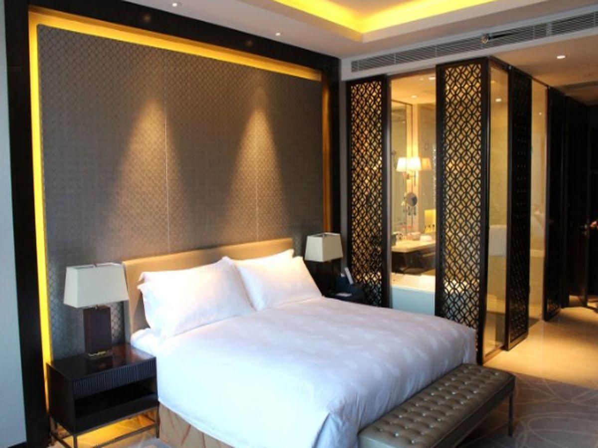 Una habitación de hotel con una cama grande, mesitas de noche, un banco y un separador decorativo.