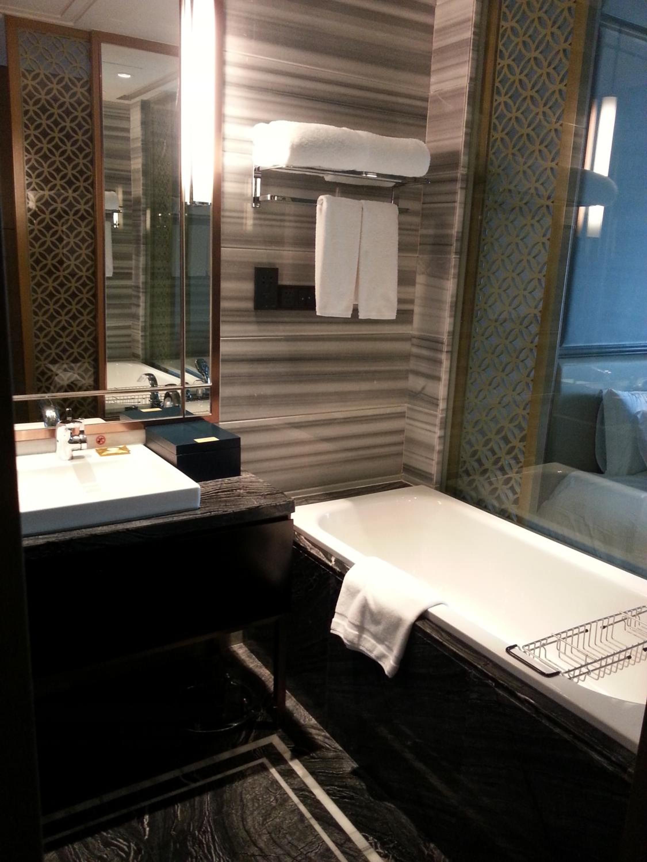 A modern bathroom with a large mirror, a sink, a bathtub, and a towel rack.