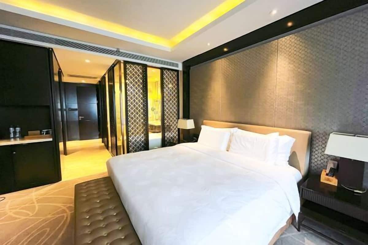 A modern hotel room with a large bed, a bedside table with a lamp, and a wardrobe.