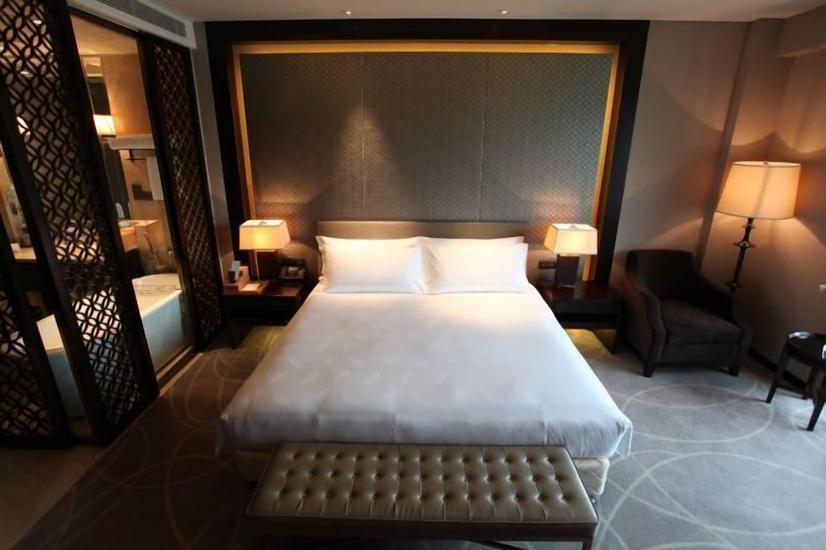 A hotel room with a large bed, two bedside lamps, a chair, and a decorative screen.