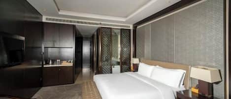 A hotel room with a bed, bedside table, lamp, TV, and a seating area with a bench.