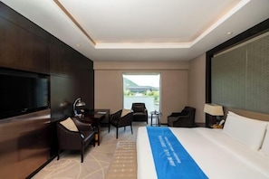 A hotel room with a large bed, a TV, a desk, and a chair.