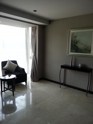 A modern hotel room with a large window, a dark armchair, a small round table, and a console table with decorative items. - Primus Hotel (Shenyang)